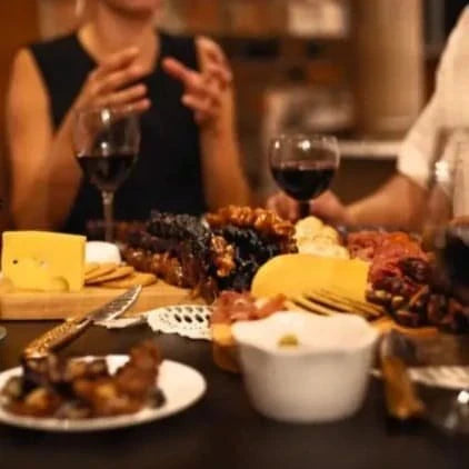 A group of friends sitting around a Charcuterie board that is filled up with Churchkhela and cheese and crackers. They all have glasses of red wine.