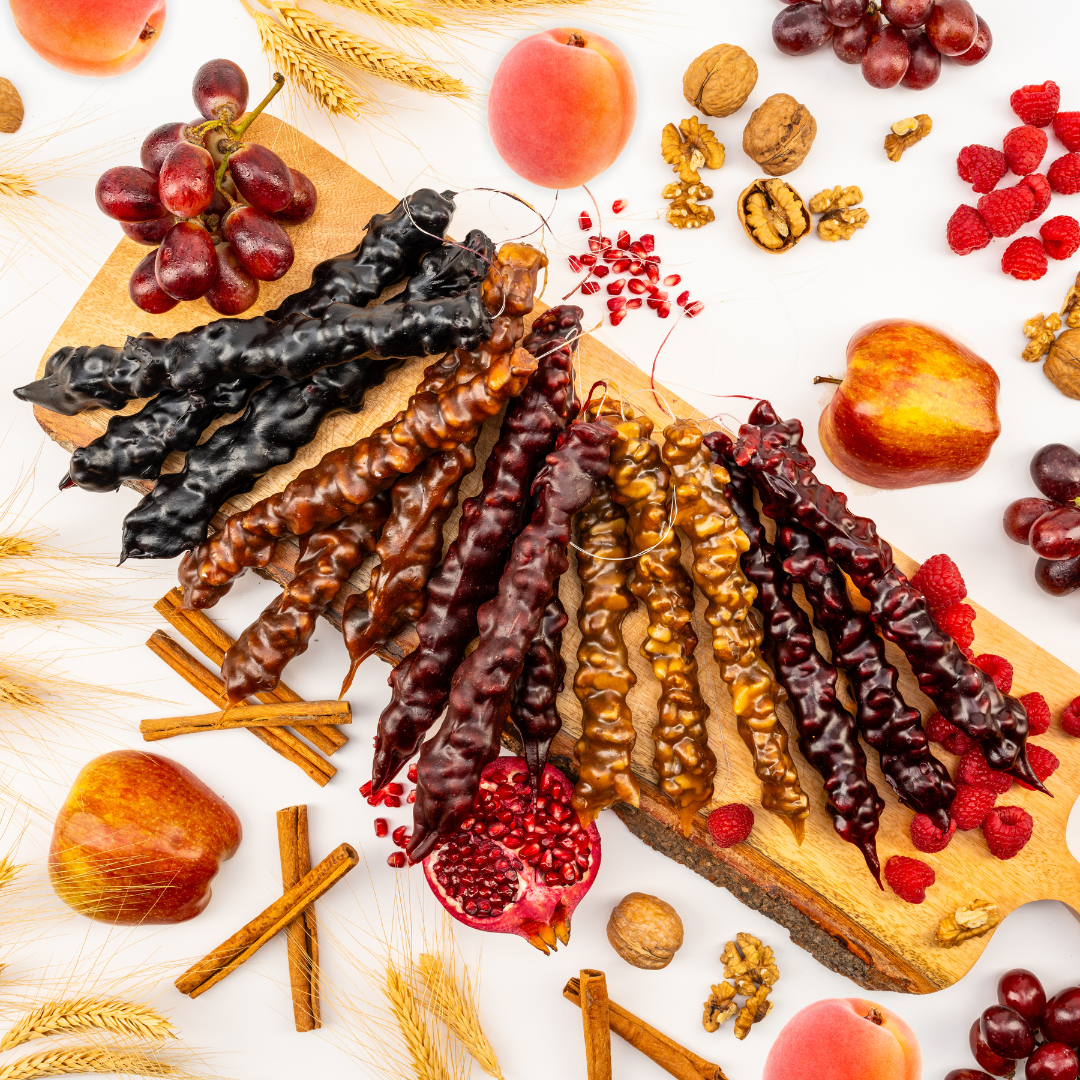 15 pack Chella Churchkhela Assorted Flavors Walnut Bundle laying on a wooden board. Three pieces of each Chella flavor: Apricot, Grape, Pomegranate, Apple Pie, and Raspberry flavors. Bundle surrounded with fresh ingredients: fruits and walnuts