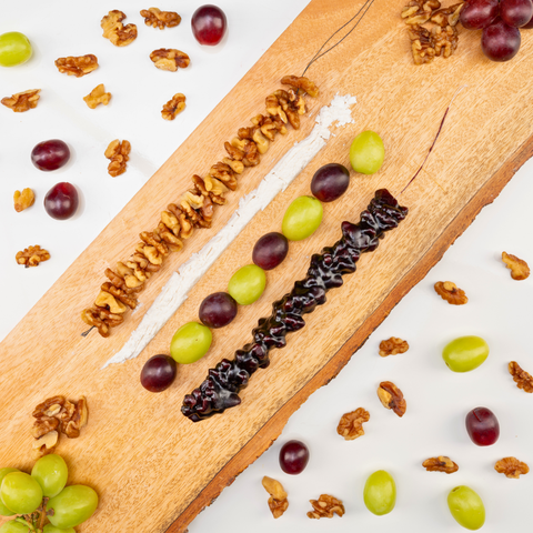 Single Walnut Grape Chella Churchkhela is laying on a wooden board, near alined ingredients: showcasing string of walnuts, line of flour, and line of grapes paralleled with Churchkhela
