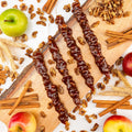 Apple Pie Walnut Chella Churchkhela on a wooden board with fresh apples, walnuts, and cinnamon sticks, highlighting healthy dessert option.