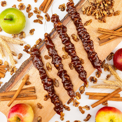 Apple Pie Walnut Chella Churchkhela on a wooden board with fresh apples, walnuts, and cinnamon sticks, highlighting healthy dessert option.