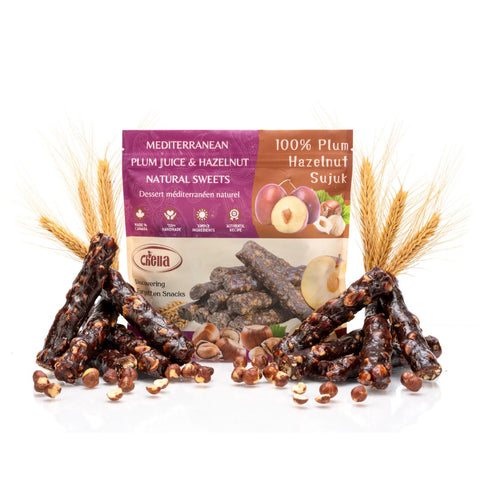 Package of Chella FruityNuts Bar plum and hazelnut flavour surrounded by clusters of shiny bars and wheat stalks on a white background.