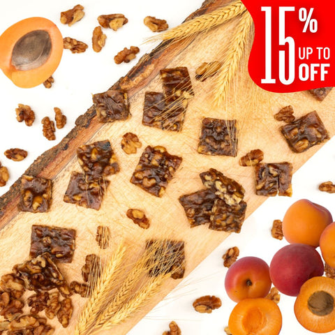 Squares of Apricot Walnut Chella FruityNuts Bites on a wooden board with apricots, wheat stalks, and a “15% off” label in the corner. Rustic and appetizing.