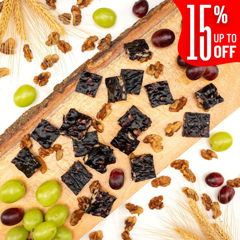 Squares of Grape Walnut Chella FruityNuts Bites on a wooden board with grapes, wheat stalks, and a “15% off” label in the corner. Rustic and appetizing.