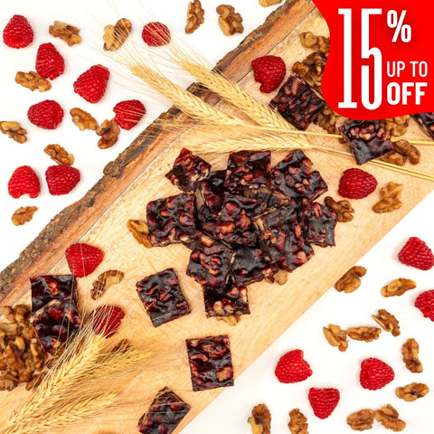 Squares of Raspberry Walnut Chella FruityNuts Bites on a wooden board with raspberries, wheat stalks, and a “15% off” label in the corner. Rustic and appetizing.