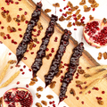 Four churchkhelas lie on a rustic wooden board, surrounded by wheat, walnuts, and pomegranates.