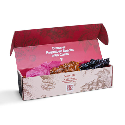 Open snack box with "Discover Forgotten Snacks with Chella" text, filled with colorful treats and pink tissue paper. Box has contact info and decorative sketches.