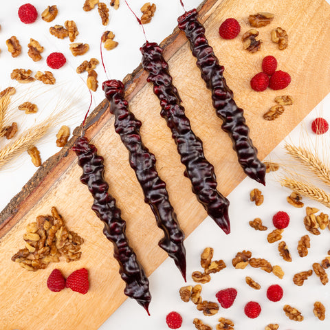 Four Churchkhelas lie on a wooden board surrounded by raspberries, wheat and walnuts.